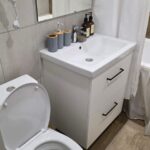 Современная ванная комната: унитаз, раковина с зеркалом и туалетные принадлежности.