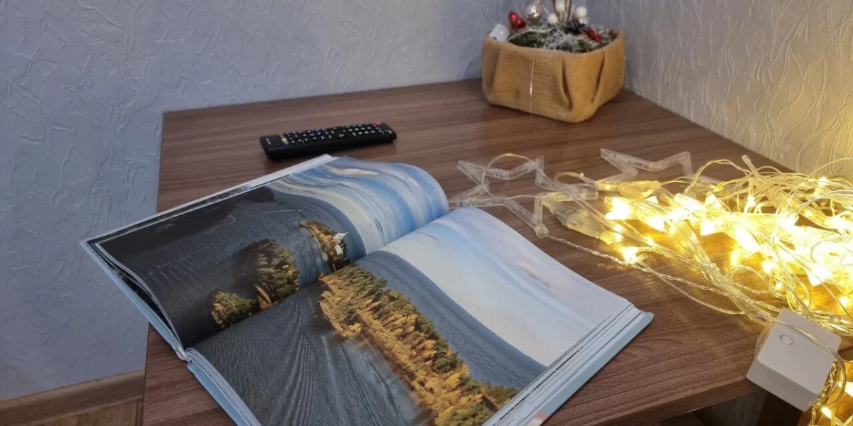 Открытая книга с фотографиями природы на столе, рядом пульт от телевизора и гирлянда из светящихся звезд.