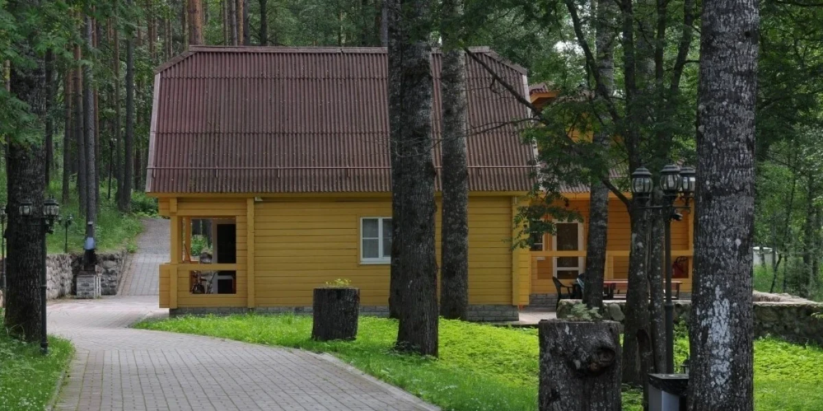 Деревянный домик с красной крышей, окруженный зелеными деревьями и освещением, расположенный на благоустроенной дорожке в лесу.
